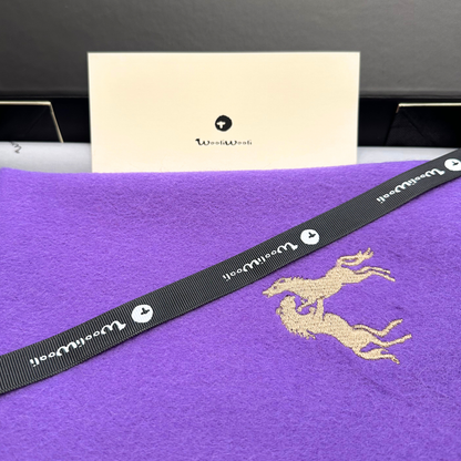 Black strap with gold horse logo on a purple scarf, with a beige card in the background.