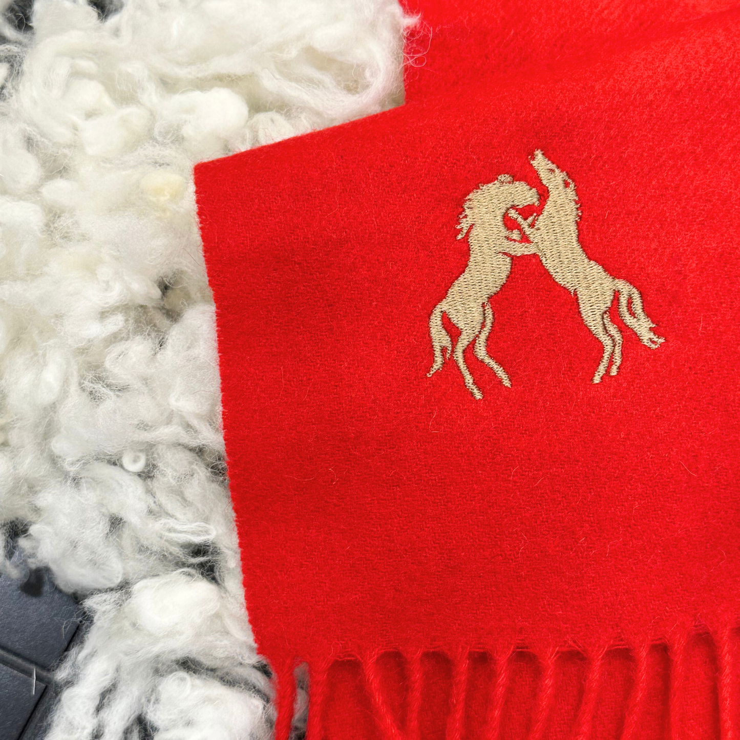 Red scarf with embroidered horse design on a textured white surface