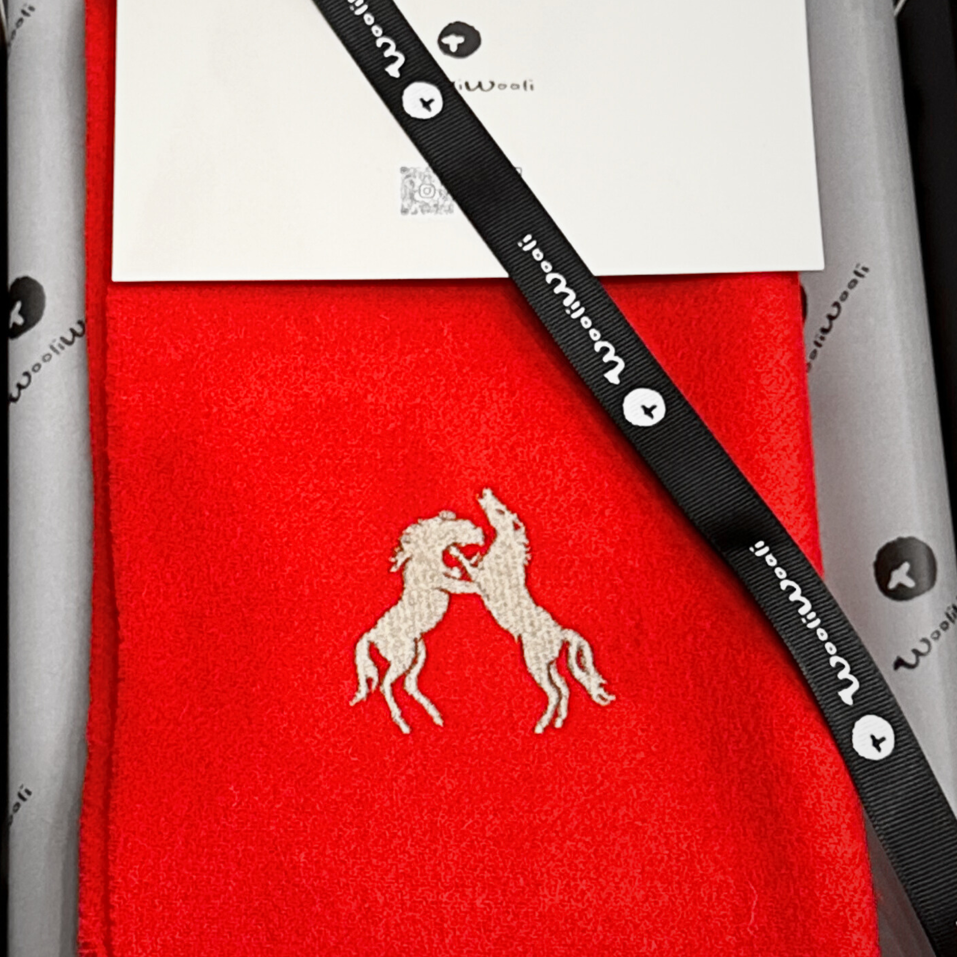 Red scarf with a gold horse emblem and a black strap on it.