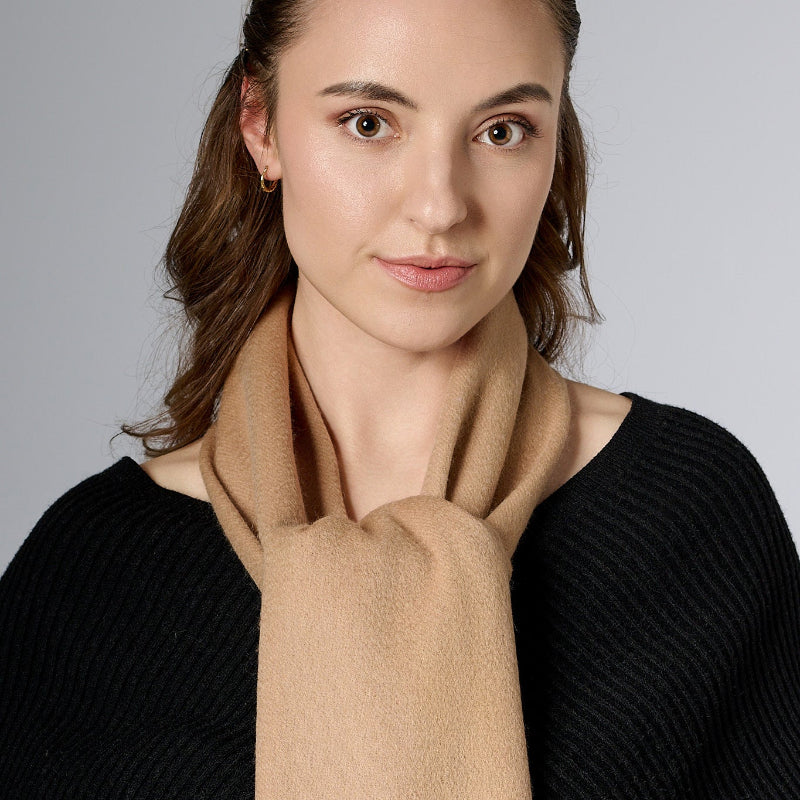 A woman wearing a light beige scarf with a neutral facial expression, looking straight ahead.