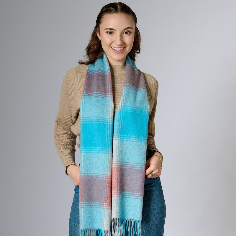 A woman wearing a multi-colored plaid scarf in shades of blue, pink, and white, paired with a beige top and blue jeans.