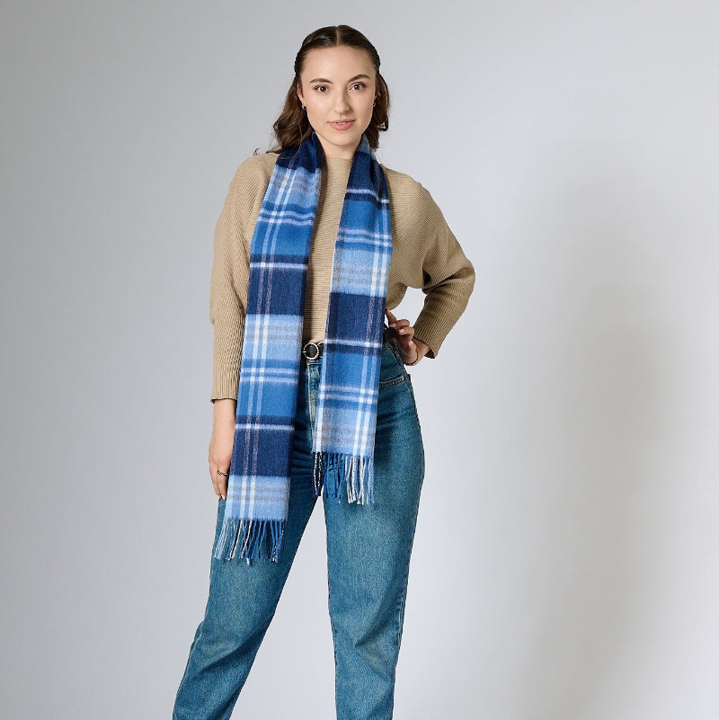 Woman wearing a blue plaid scarf, beige cardigan, and jeans on a white background