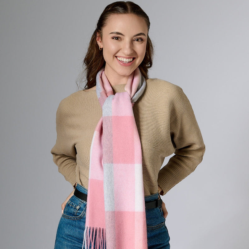 A woman wearing a beige cardigan and blue jeans, accessorized with a blush pink and white plaid scarf with fringes.