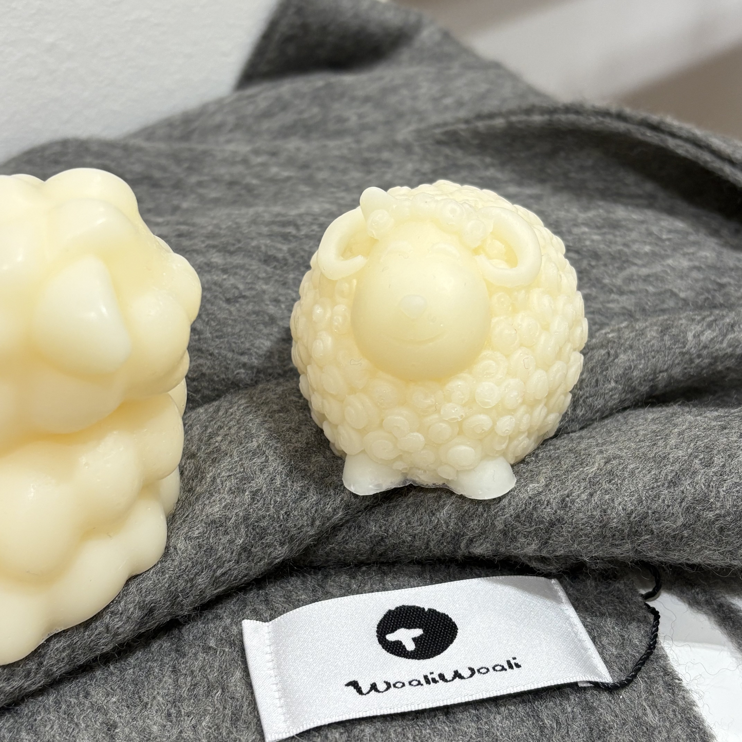 Two white mini handmade goat soap on a gray fabric surface with a visible brand label.