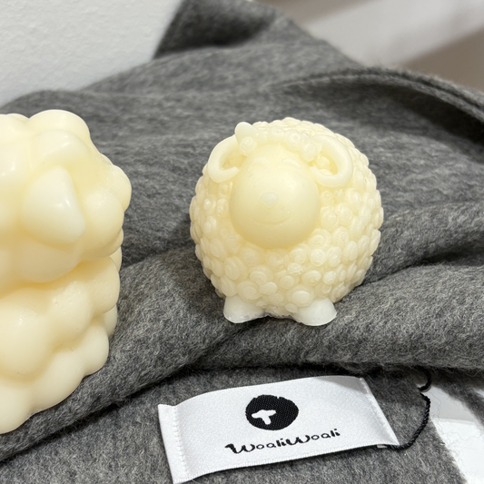 Two white mini handmade goat soap on a gray fabric surface with a visible brand label.