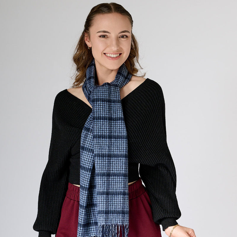 A woman wearing a black off-shoulder top and red trousers, accessorized with a pin check-patterned navy scarf.