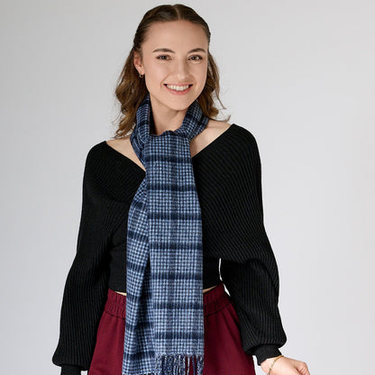 A woman wearing a black off-shoulder top and red trousers, accessorized with a pin check-patterned navy scarf.