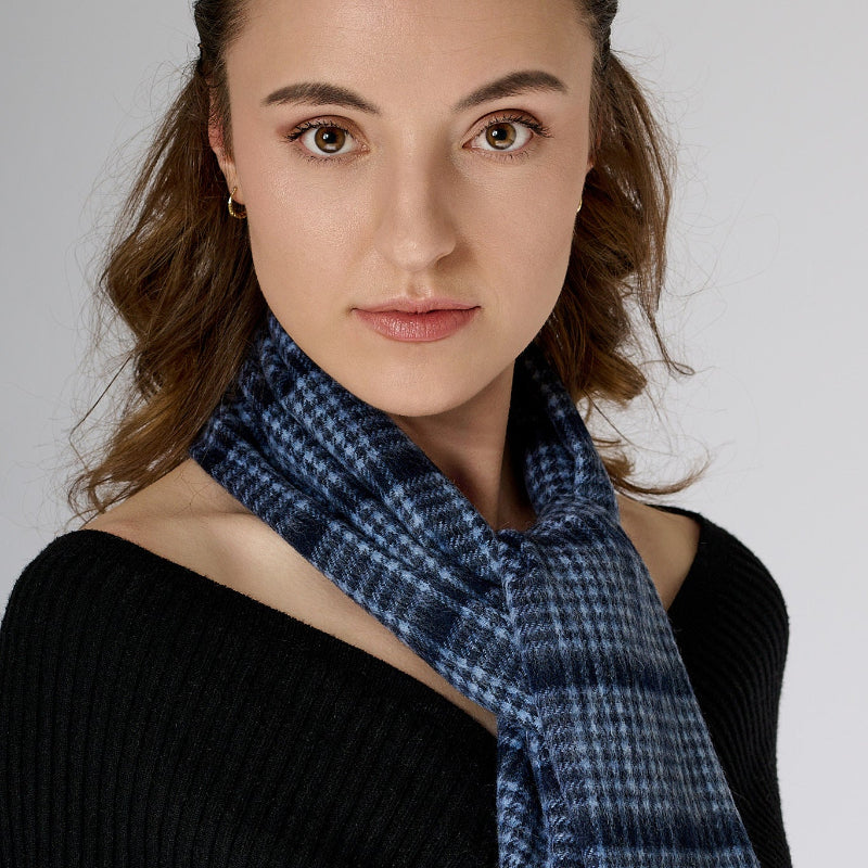 A woman wearing a black off-shoulder top and red trousers, accessorized with a pin check-patterned navy scarf.