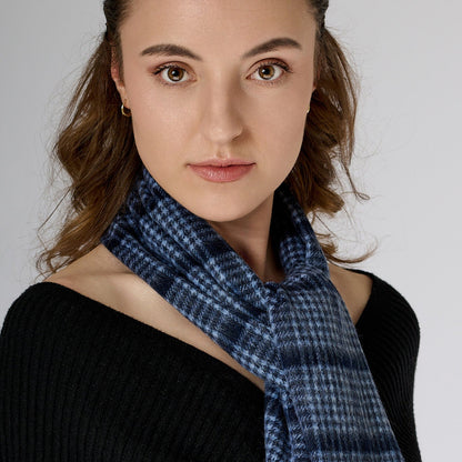 A woman wearing a black off-shoulder top and red trousers, accessorized with a pin check-patterned navy scarf.