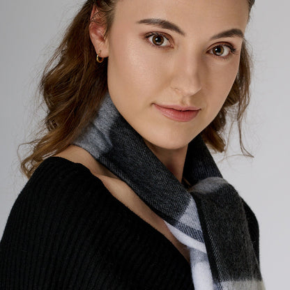 Woman wearing a black sweater and gray scarf against a plain background