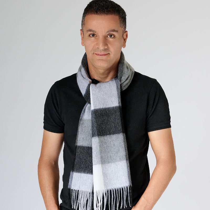 A man wearing a black t-shirt and black pants, with a black and grey plaid merino wool scarf wrapped around his neck.