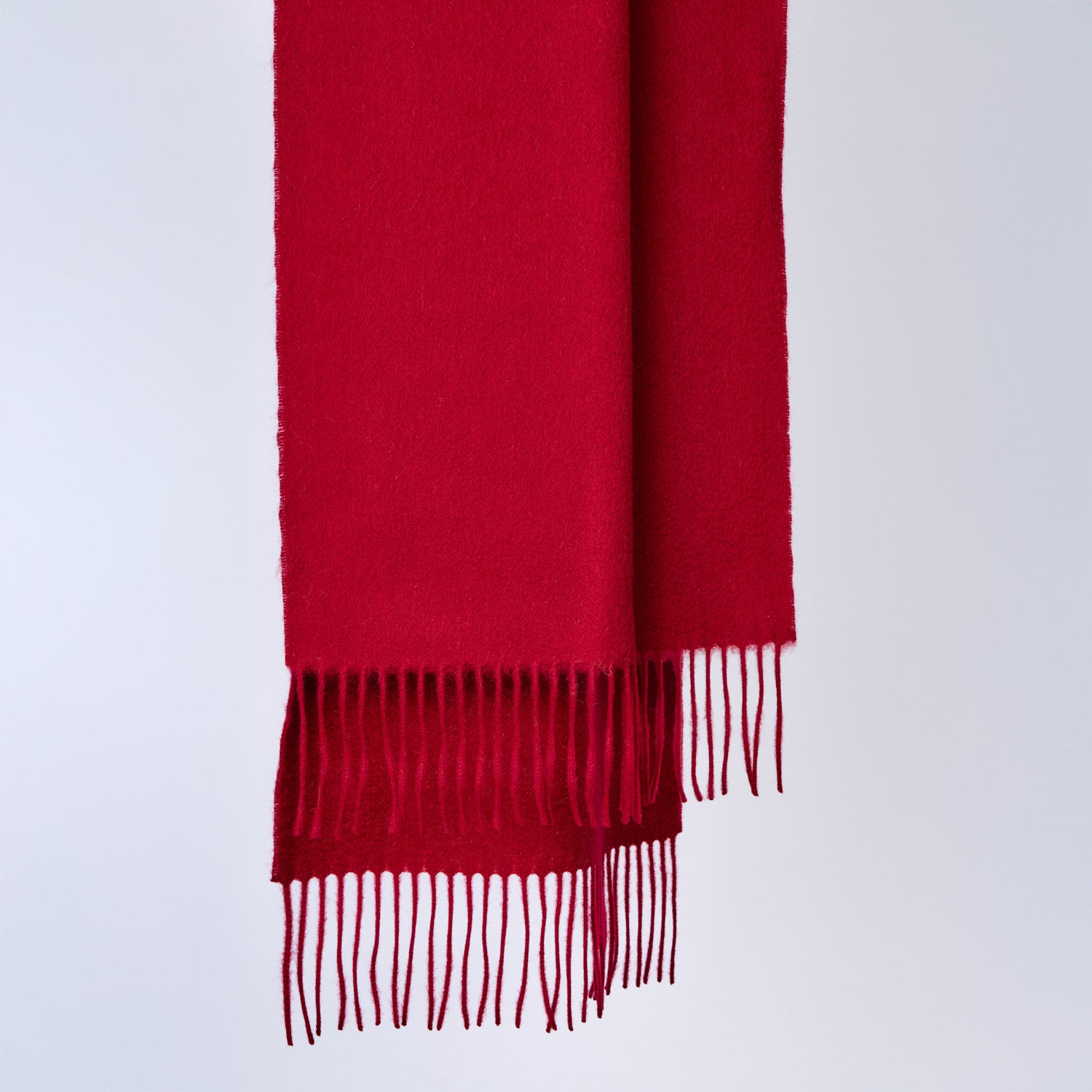 Burgundy red wool scarf with fringes on a light gray background