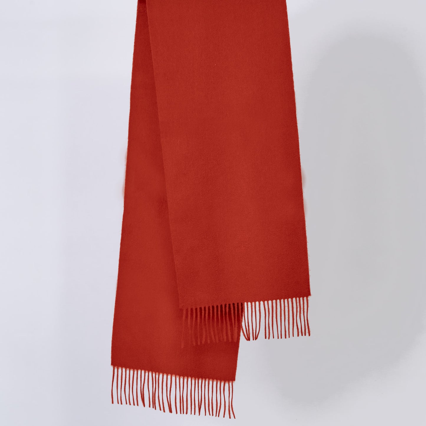 Pumpkin-red wool scarf with fringes on a light gray background
