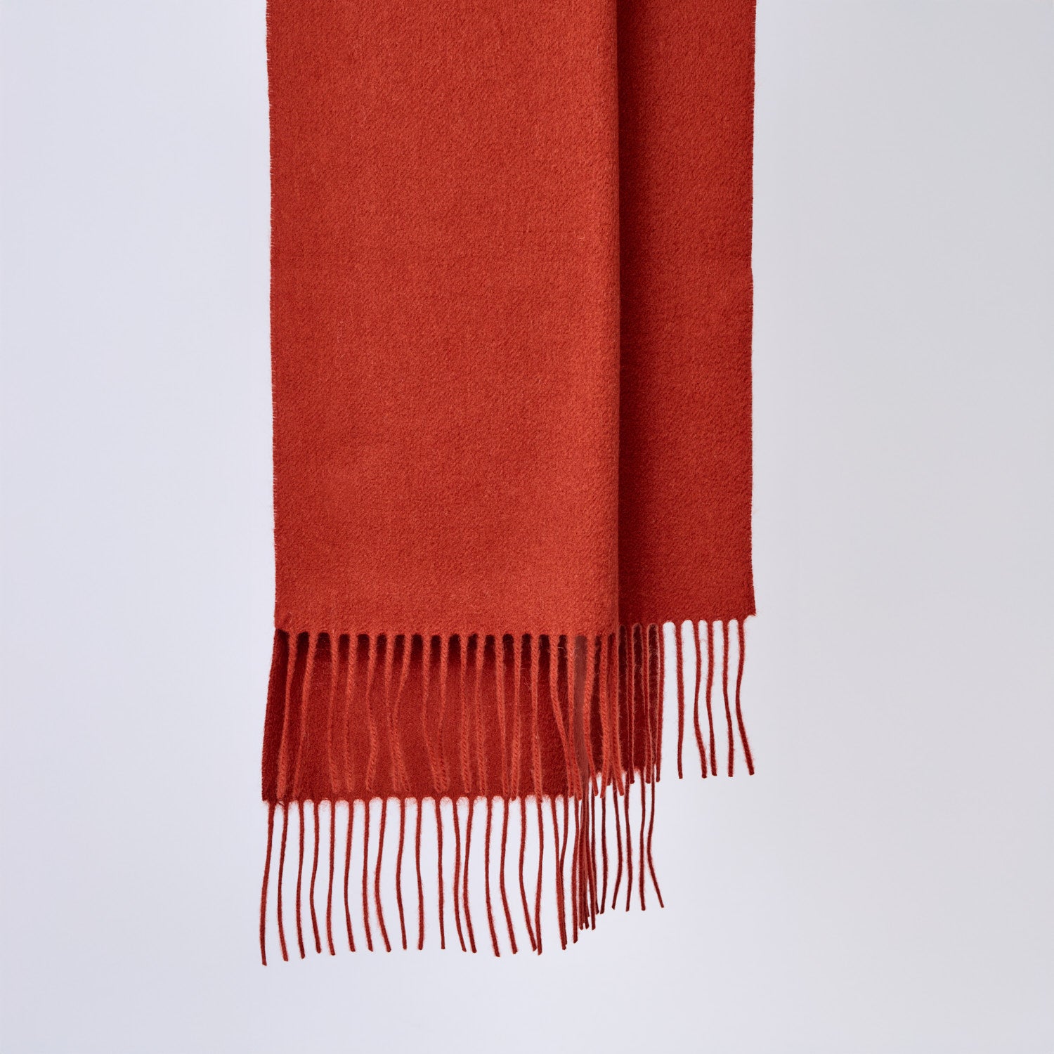 Pumpkin red wool scarf with fringes on a light gray background