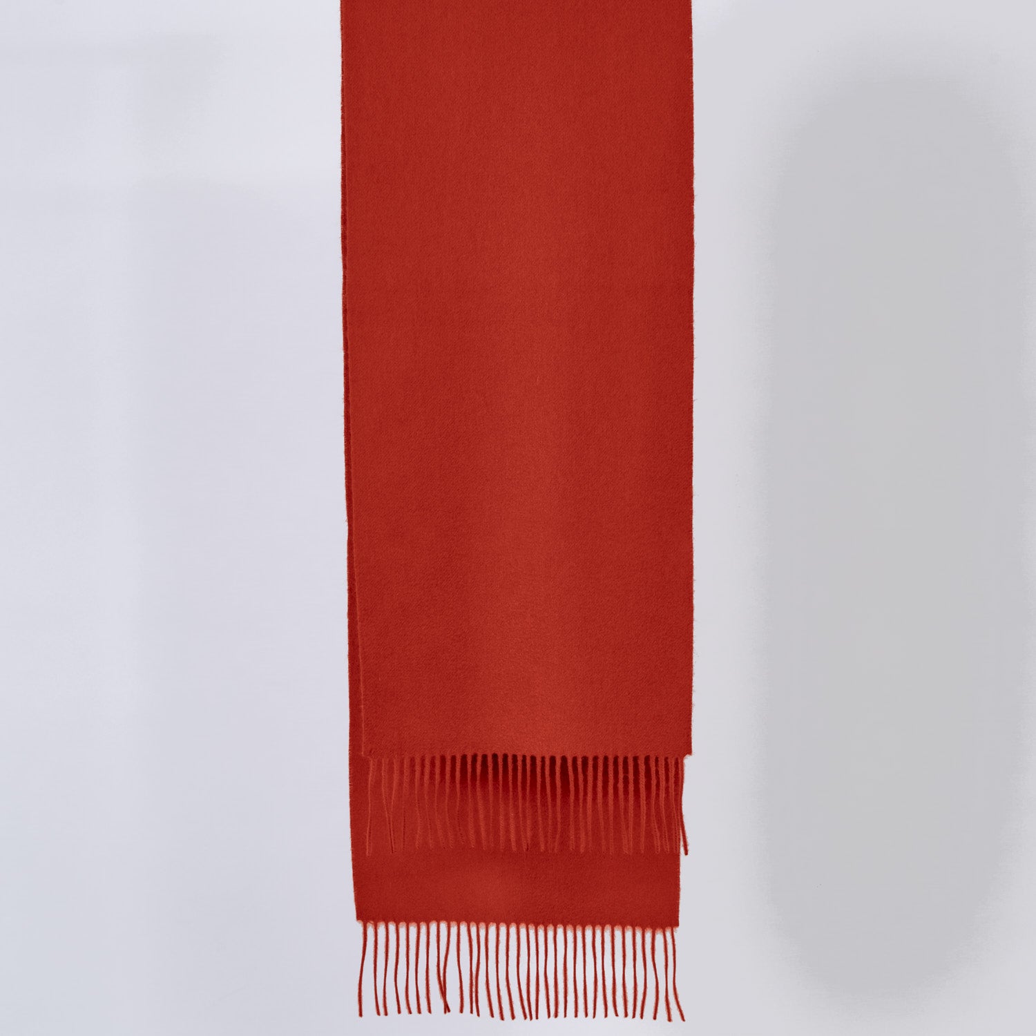 Pumpkin red scarf with fringes on a light gray background
