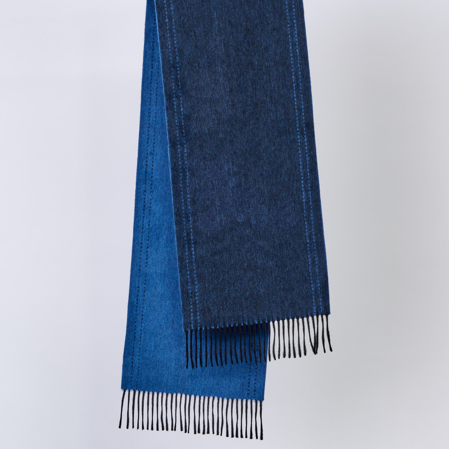 Blue wool scarf with black fringe on a light gray background
