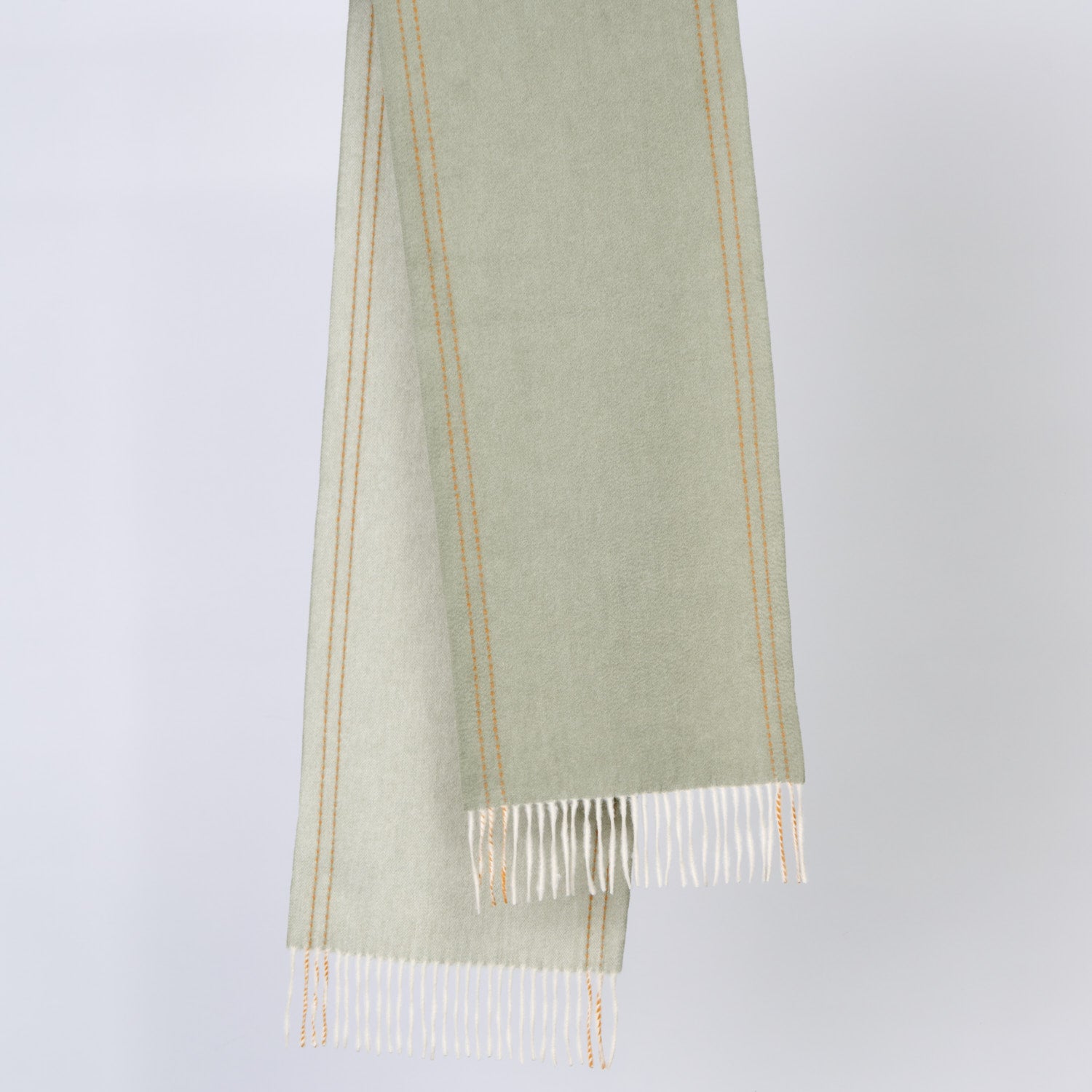 Green wool scarf with white fringe on a light gray background