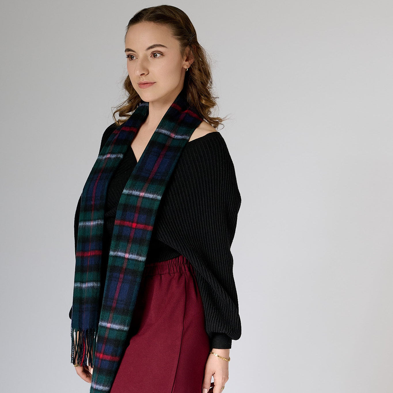 A woman wearing a black top and a maroon skirt, draped with a plaid scarf in green, blue, and white over her shoulders.