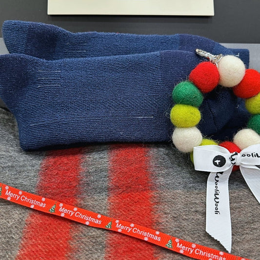 Blue socks with a colorful beaded bracelet on a gray surface with a 'Merry Christmas' ribbon.