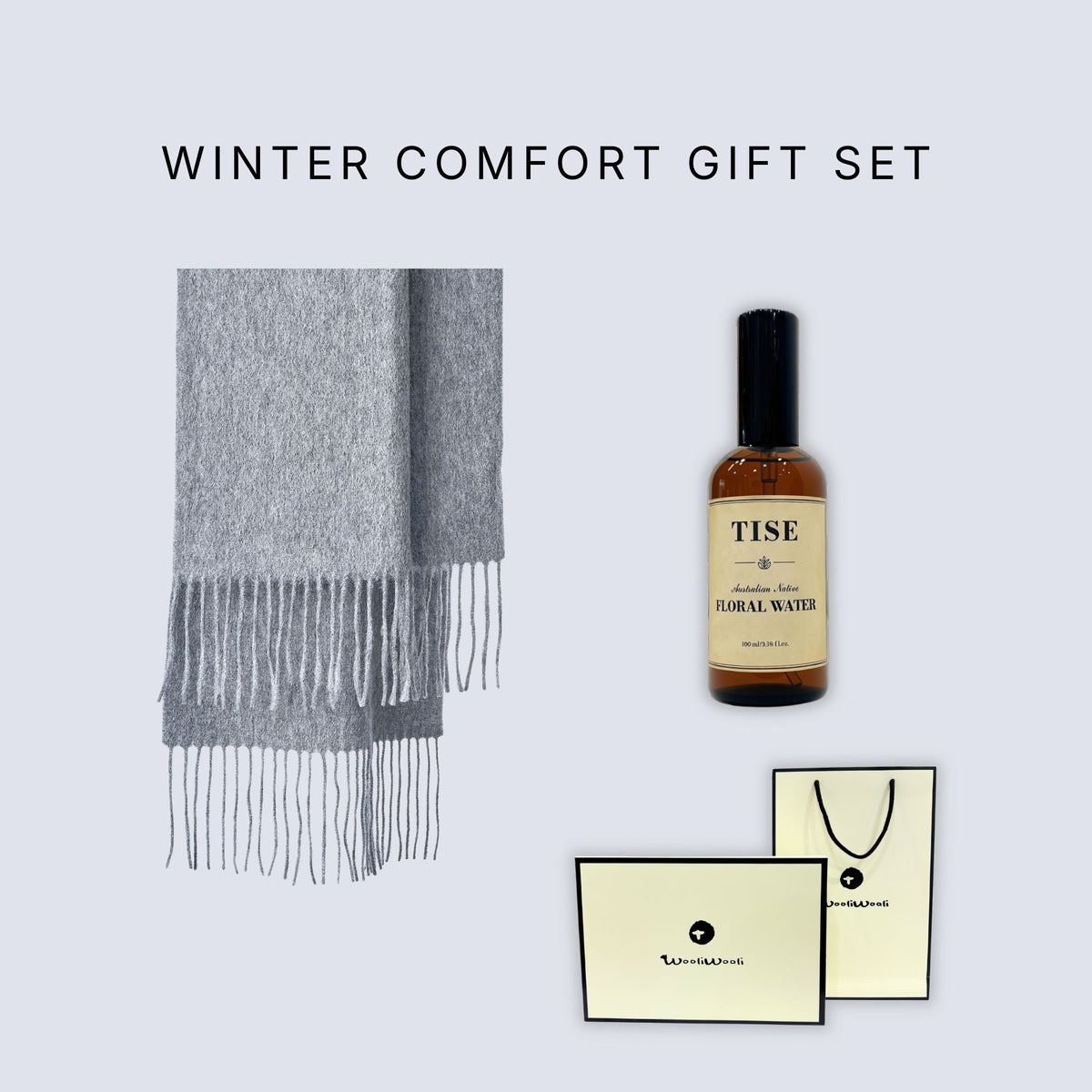 Winter Comfort Gift Set featuring a light gray fringed scarf, a bottle of Tise herbal floral water, and branded cream-colored gift cards and a shopping bag on a light gray background.