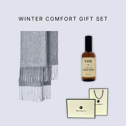 Winter Comfort Gift Set featuring a light gray fringed scarf, a bottle of Tise herbal floral water, and branded cream-colored gift cards and a shopping bag on a light gray background.