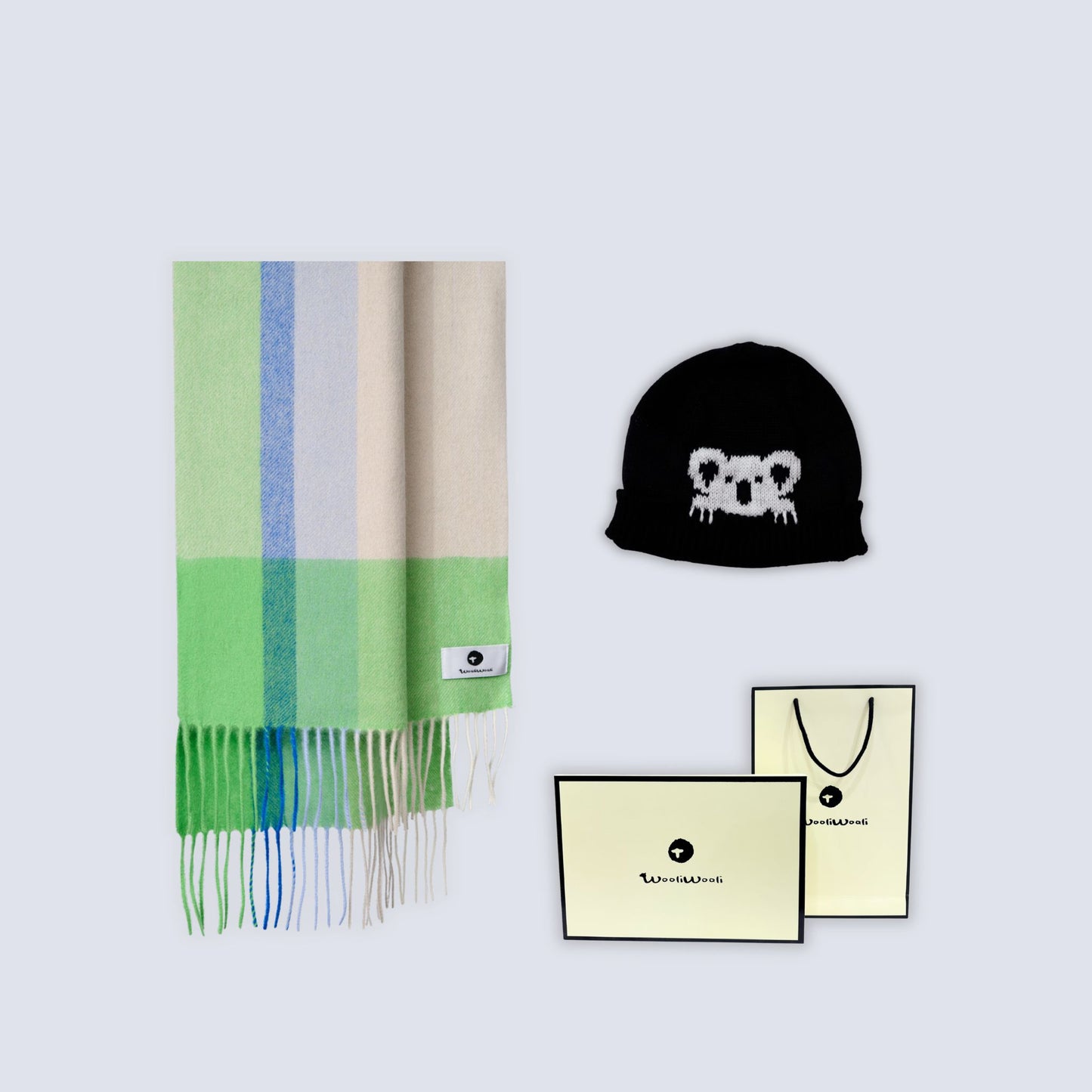 A flat-lay product shot featuring a multicolor striped wool scarf with fringe, a black beanie with a white koala graphic, and two branded cream-colored shopping bags from Kaviar, set against a solid light gray background.