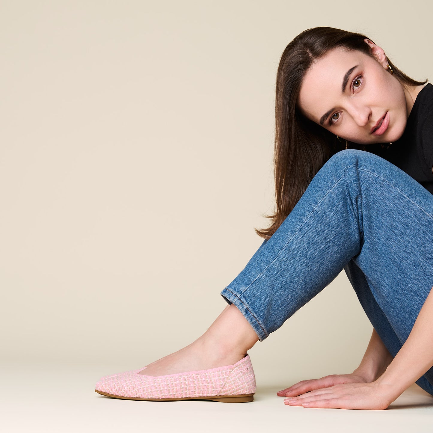 Woman wearing pink checkered flats and blue jeans sitting on a beige background