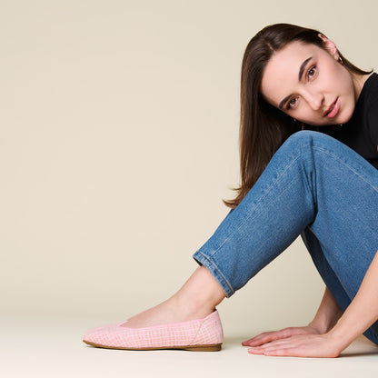 Woman wearing pink checkered flats and blue jeans sitting on a beige background