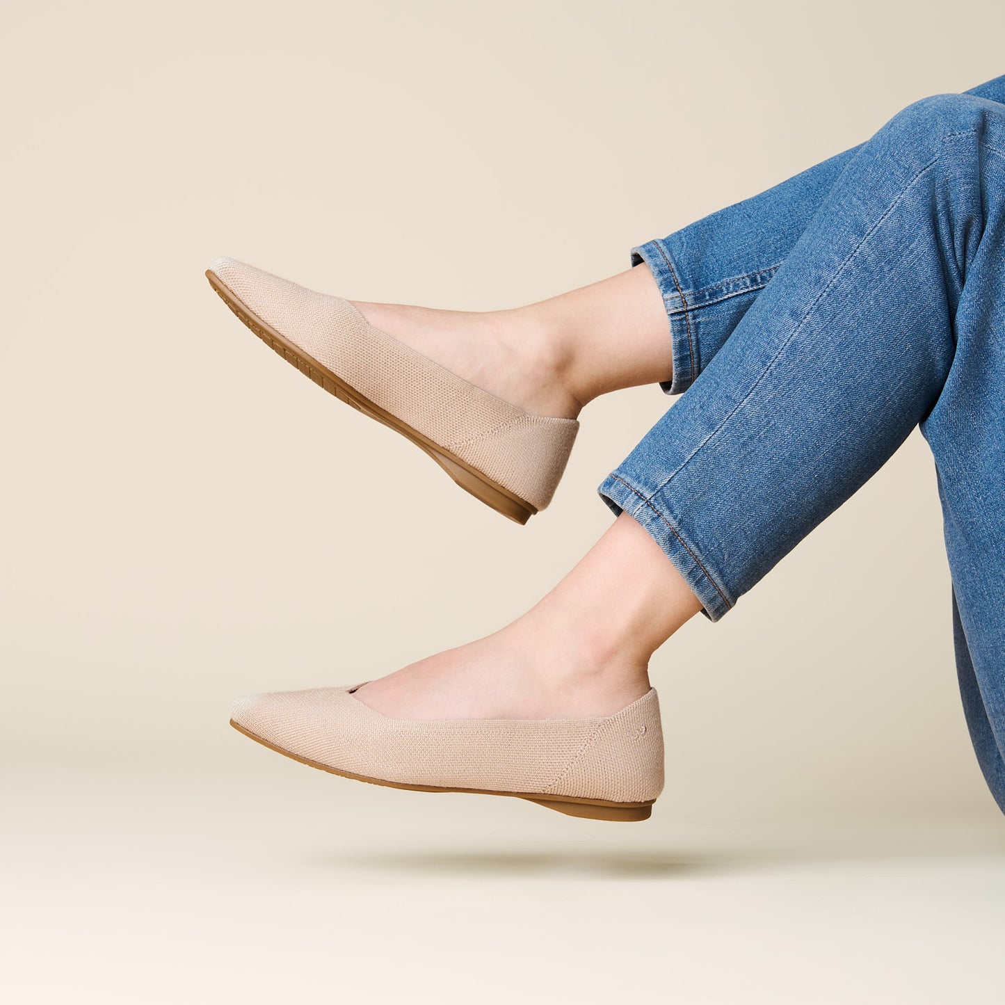 Beige flats worn with blue jeans on a beige background