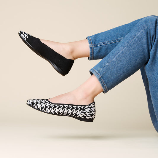 Black and white patterned flats worn with blue jeans on a beige background