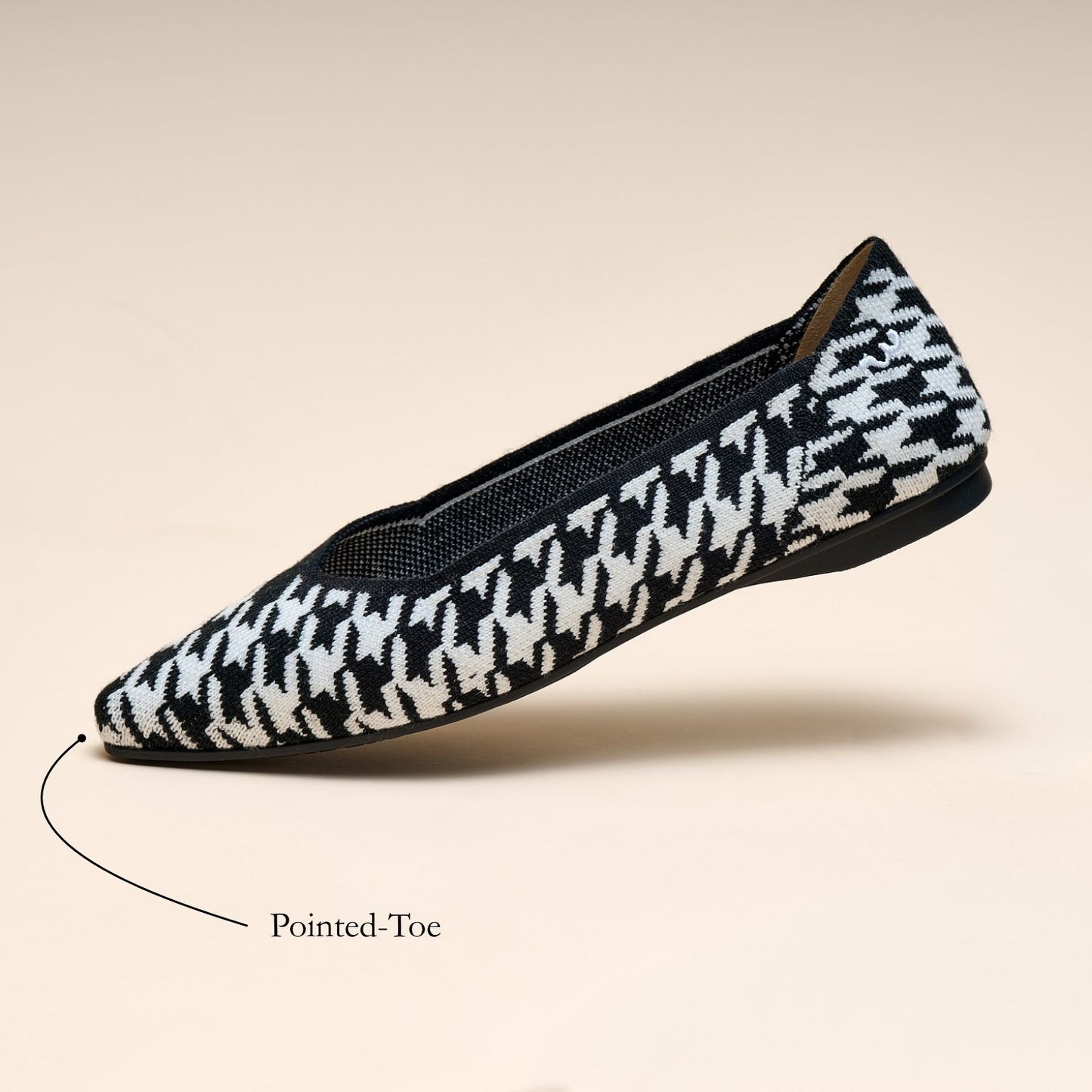 Black and white houndstooth patterned pointed-toe flat shoe on a beige background