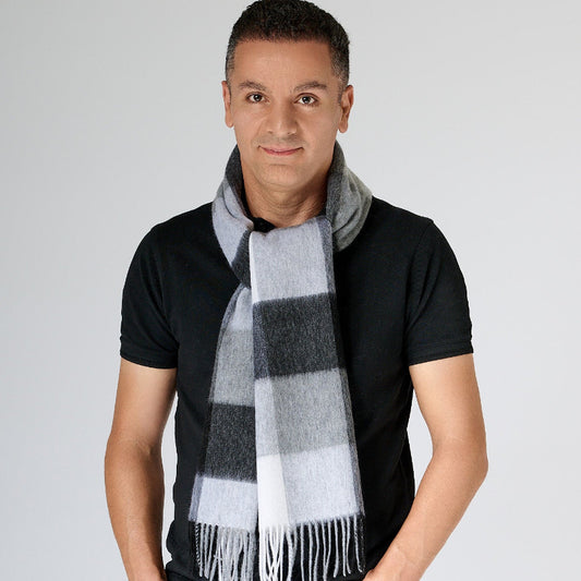 A man wearing a black t-shirt and black pants, with a black and grey plaid merino wool scarf wrapped around his neck.